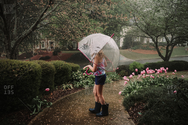 Young girl walking on path with umbrella in the rain in springtime