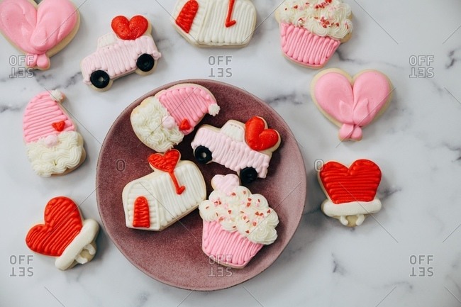 Variety of Valentine\'s Day sugar cookies on white marble surface and plate