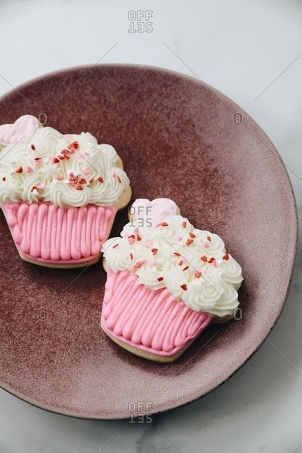Two cupcake shaped sugar cookies on white marble surface