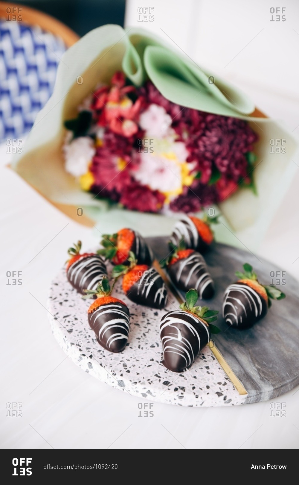 Gourmet chocolate covered strawberries on stone platter beside bouquet of flowers
