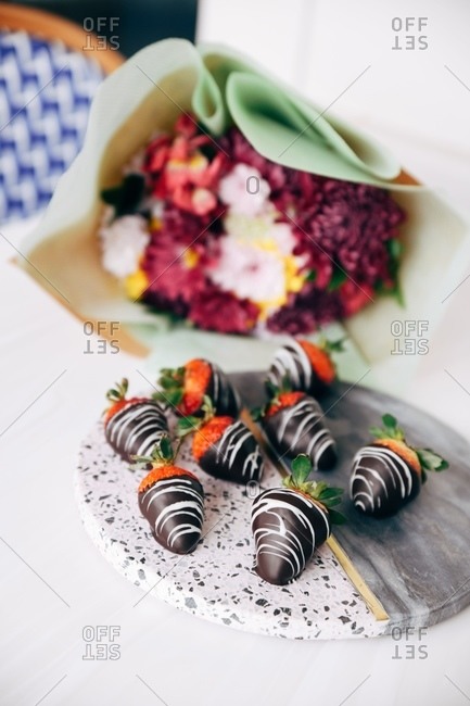 Gourmet chocolate covered strawberries on stone platter beside bouquet of flowers