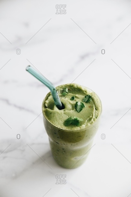 A green healthy smoothie on white marble surface with straw