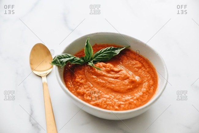 Tomato soup with basil on white marble surface with gold utensils