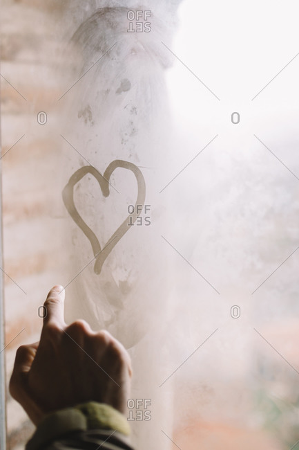 Man drawing with his finger a heart in wet window