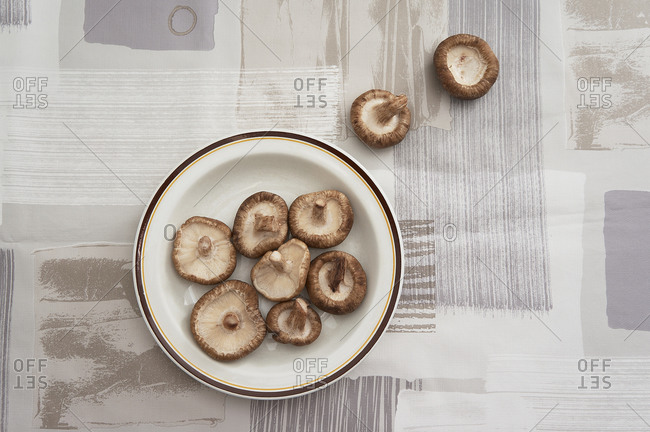 Top view of a plate with raw mushrooms placed on a brown tablecloth