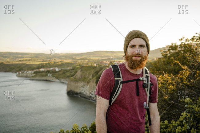Smiling bearded man with view of robins hood's bay behind at sun