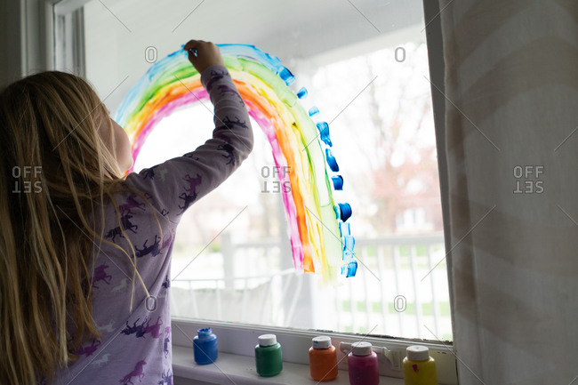Back view of blond girl painting rainbow on window