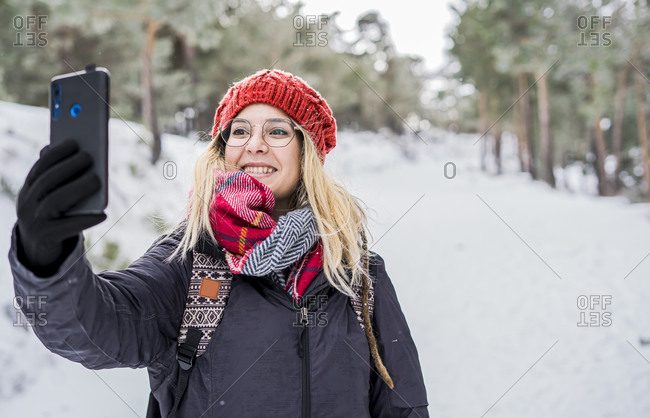Smiling girl enjoying winter and taking selfie while snowing