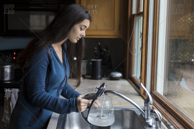 Pretty teen girl filling kettle with water in kitchen sink