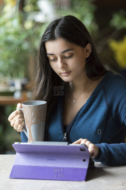 Pretty teen girl working on tablet and holding coffee cup