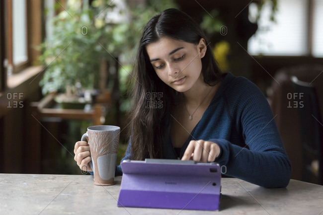 Pretty teen girl working on tablet and holding coffee cup