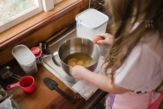 Girl wearing an apron and cracking eggs into a bowl in the kitchen