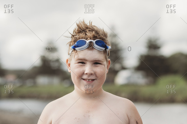 Smiling boy at the beach with goggles on the top of his head