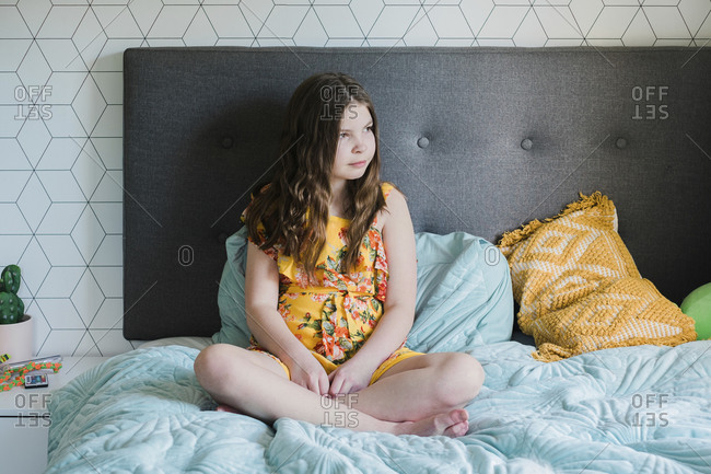 Young girl sitting cross legged on a bed resting against a head board
