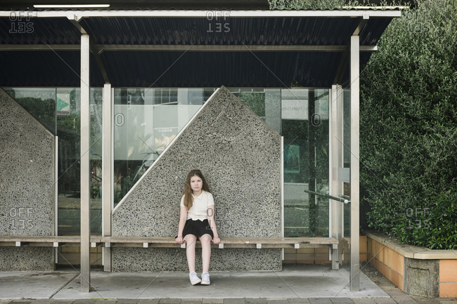 Young girl sitting alone on a wooden seat at a bus stop