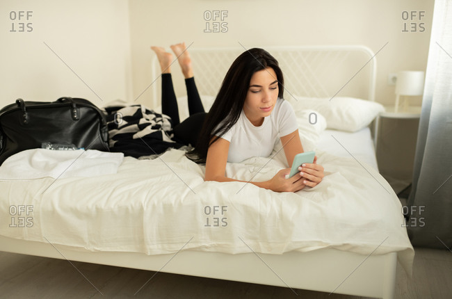Attractive female lying on bed with smartphone