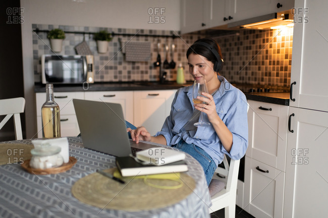 Woman drinking wine and using laptop in kitchen