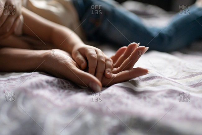 Cropped mother and child holding hands on bed