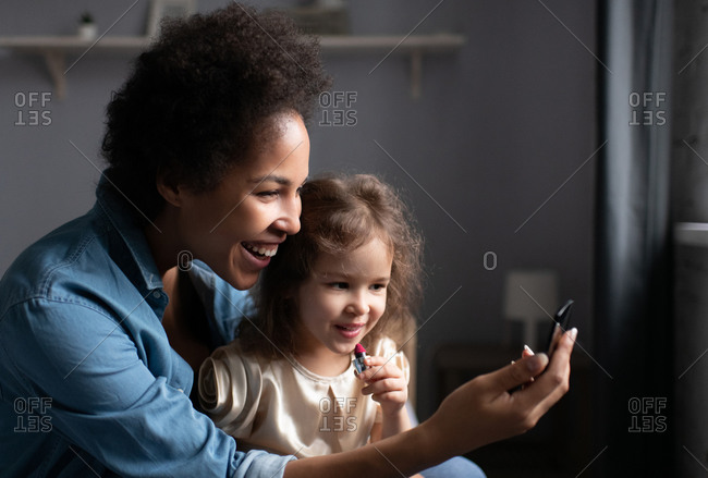 Happy ethnic woman teaching daughter to apply lipstick