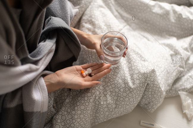 Crop ill woman taking pills in bed