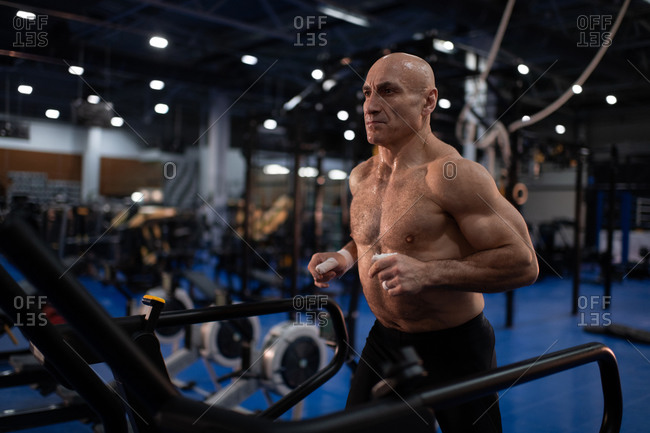 Muscular senior sportsman running on treadmill