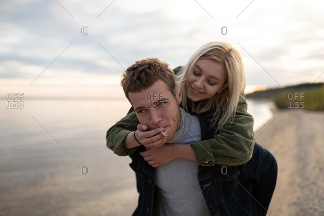 Smiling woman sharing cigarette to boyfriend near lake