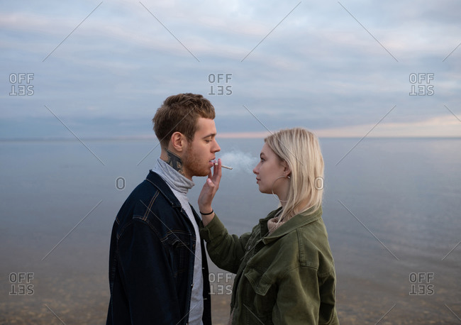 Sensual young hipsters sharing joint on dusky coast