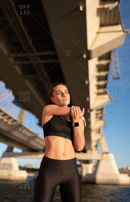Woman stretching arms standing on seafront under bridge