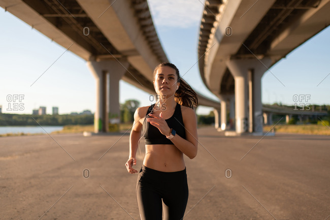 Young sportswoman in headphones jogging on spacious seafront