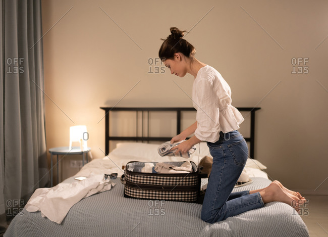 Young female putting clothes in suitcase