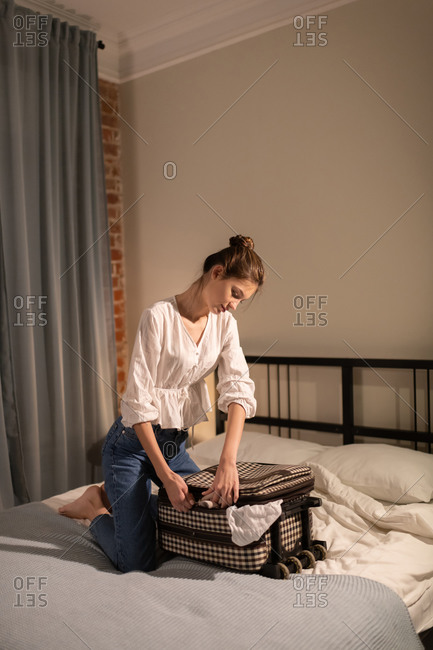 Young female closing suitcase on bed before trip