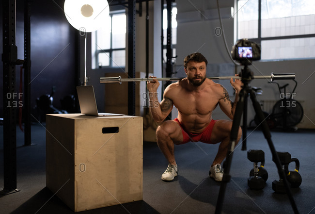 Sportsman doing squats with bar in front of camera