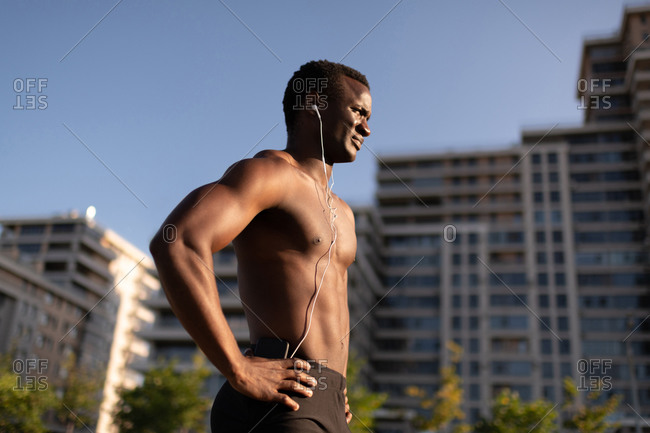 Muscular man with naked torso smartphone and earphones outside