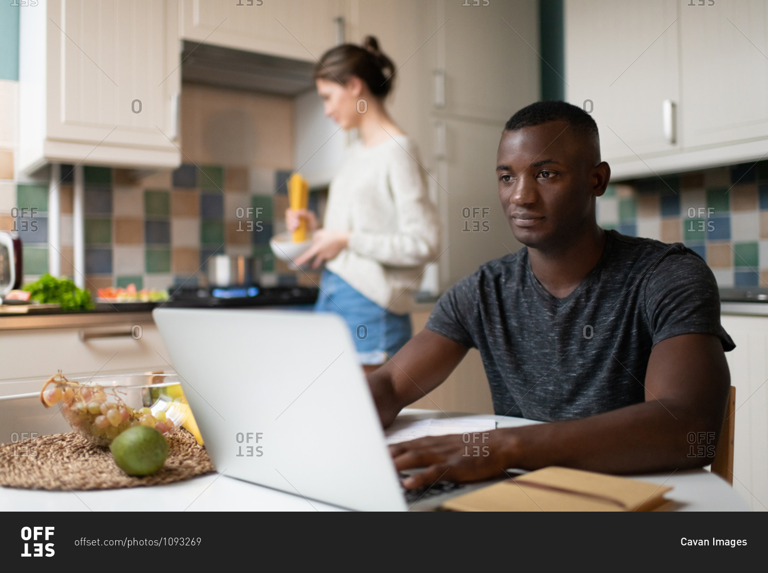 Smart black man working on laptop near cooking girlfriend
