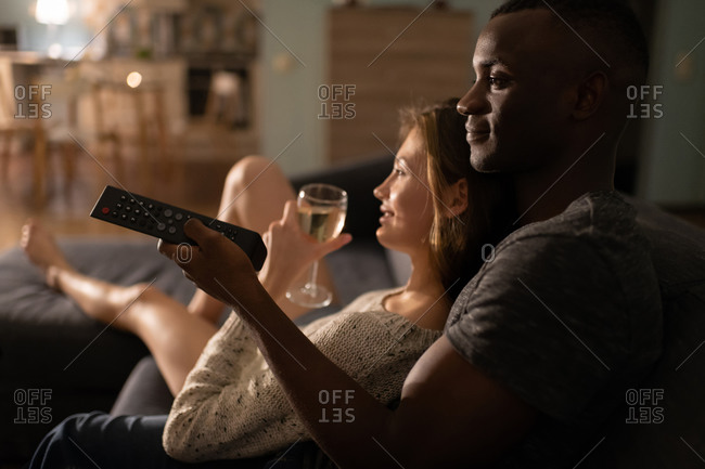 Multiethnic couple with wineglass watching tv