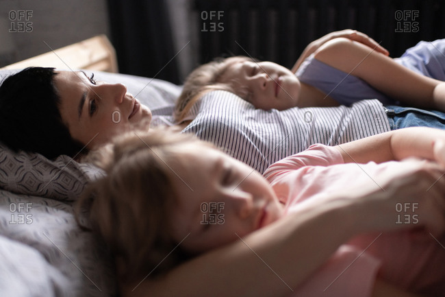 Mother hugging sleeping daughters in morning at home