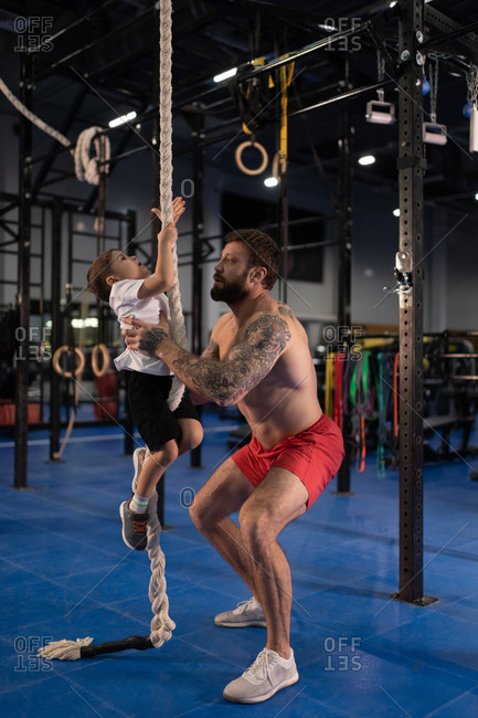 Shirtless father teaching boy to climb rope during training