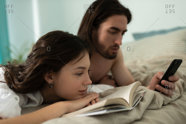 Young man looking at smartphone while his girlfriend reading boo