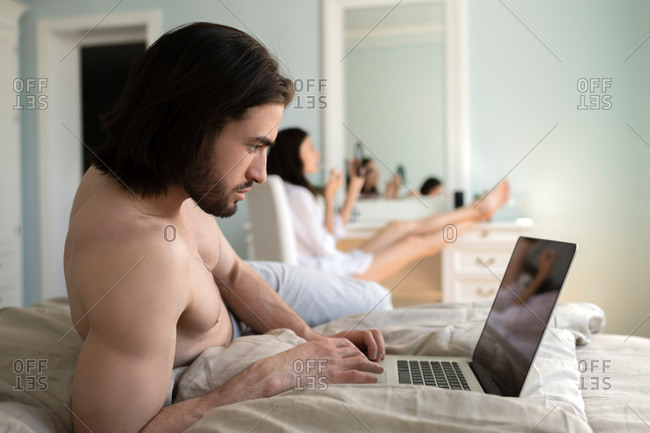 The man working on the computer while his wife  putting makeup o