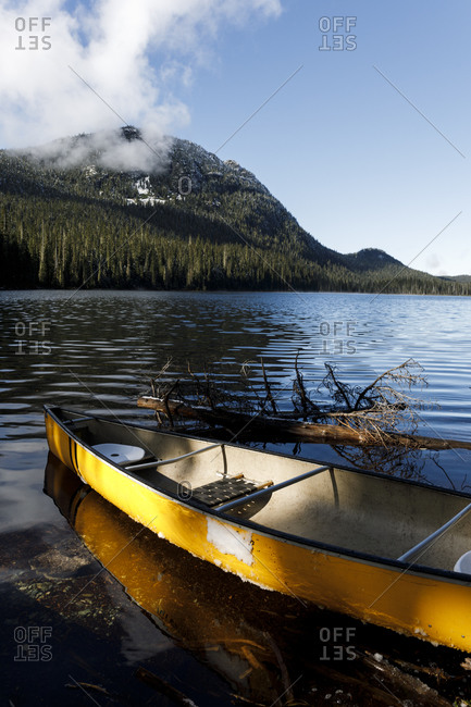 A canoe is on the shore of a lake surrounded by forest and mountain