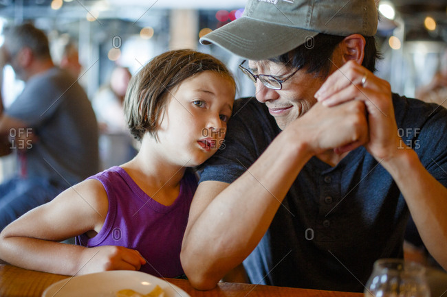 A father smiles down at child leaning on him in crowded restaurant
