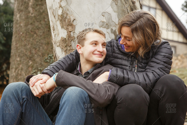 A loving mom and son lean together against large sycamore tree outside