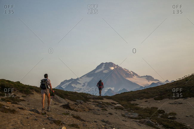 Two hikers climb towards the summit of glacier peak at dawn.