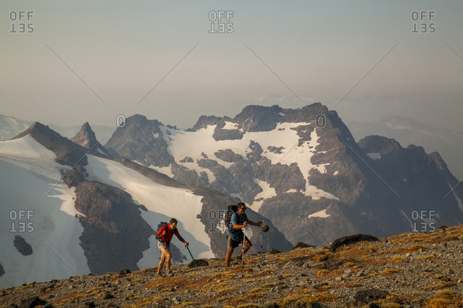 Two hikers climb towards the summit of glacier peak at dawn.