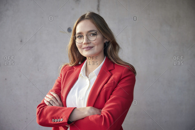 Young businesswoman standing with arms crossed against wall
