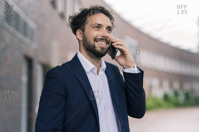 Smiling male entrepreneur talking on smart phone against building