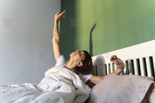 Smiling woman stretching while sitting on bed at home
