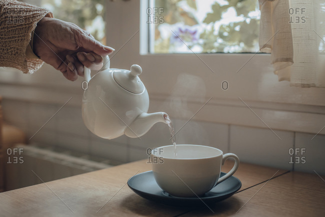 Woman's hand serving tea in cup on kitchen table
