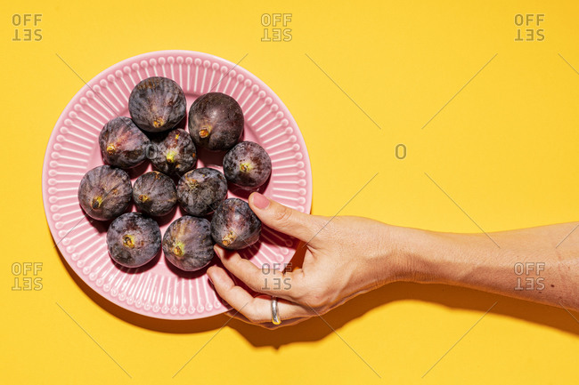 Hand of woman picking up fresh fig from plate