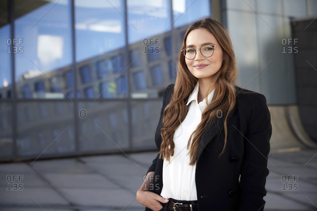Confident businesswoman wearing eyeglasses with hand in pocket standing outdoors